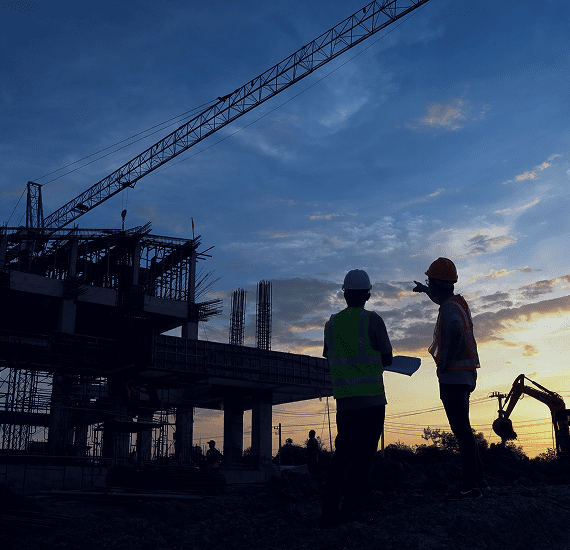 Two construction workers surveying site at sunset